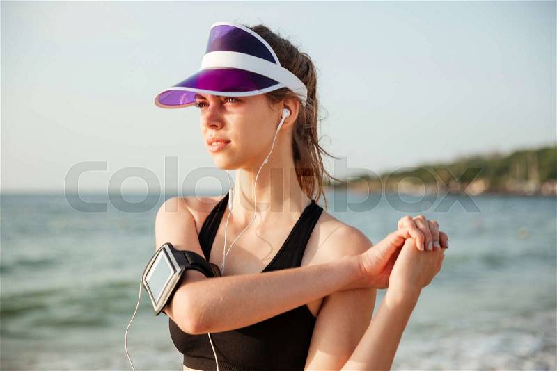 Female young fitness runner doing warm-up routine on beach before running, stock photo