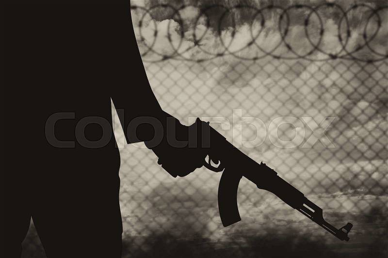 Terrorist concept. Silhouette of a terrorist near the fence of barbed wire and smoke, stock photo