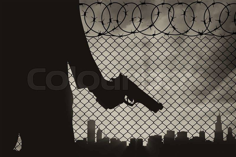 Terrorist concept. Pistol in hand terrorist, against the background of the fence of barbed wire and the city, stock photo