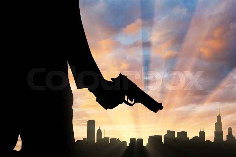 Terrorist concept. Pistol in hand terrorist, against the background of the urban landscape at sunset, stock photo