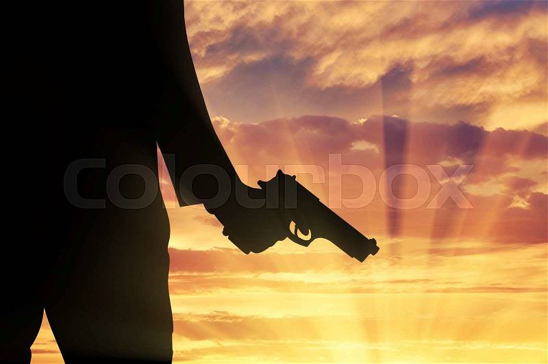 Terrorist concept. Pistol in hand terrorist on sunset background, stock photo