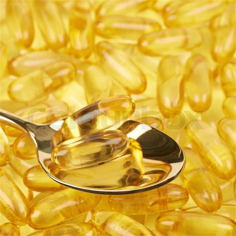 Surface covered with multiple yellow softgel pills with a metal spoon over it as a medical backdrop composition, stock photo