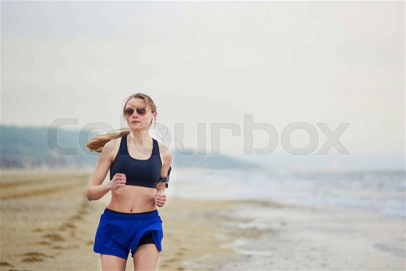 Young fitness running woman jogging fast on beach near ocean or sea on a foggy misty morning. Fitness and healthy lifestyle concept, stock photo