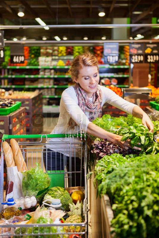 Portrait of beautiful young woman choosing green leafy vegetables in grocery store. Concept of healthy food shopping, stock photo