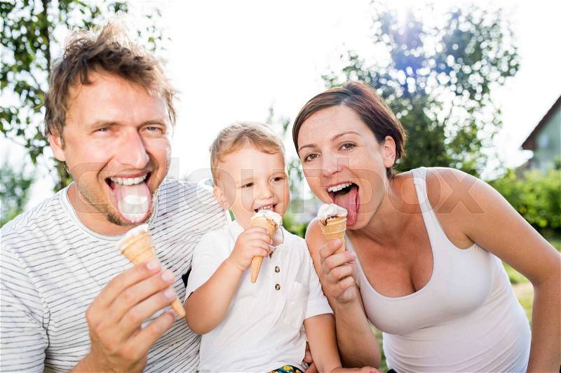 Young parents with their little son eating ice cream, sunny summer garden, stock photo