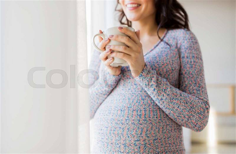 Pregnancy, drinks, rest, people and expectation concept - close up of happy pregnant woman with cup drinking tea looking through window at home, stock photo