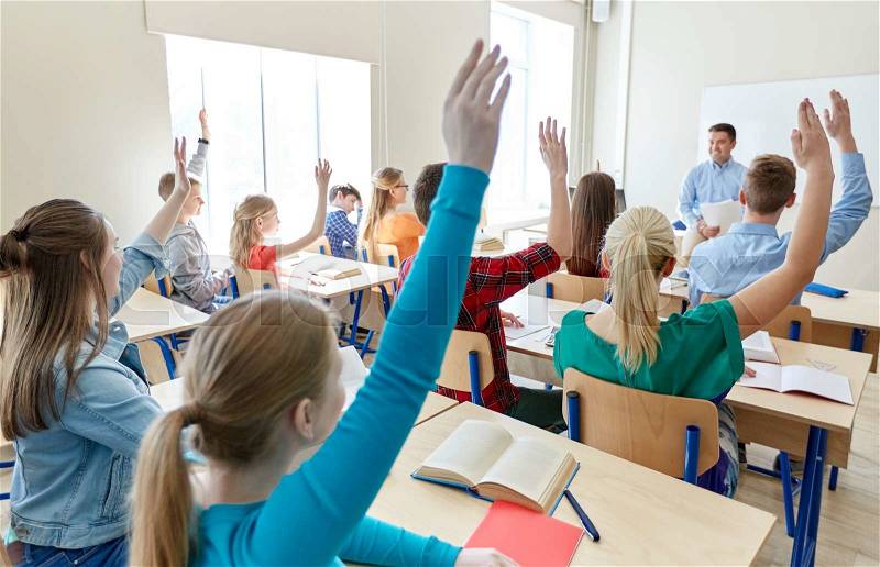 Education, high school, teaching, learning and people concept - group of happy students raising hands and teacher in classroom, stock photo