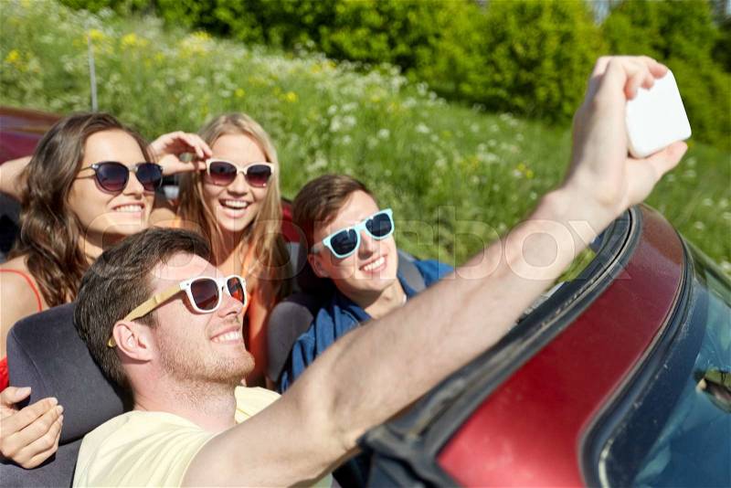 Leisure, road trip, travel and people concept - happy friends driving in cabriolet taking selfie by smartphone at country, stock photo