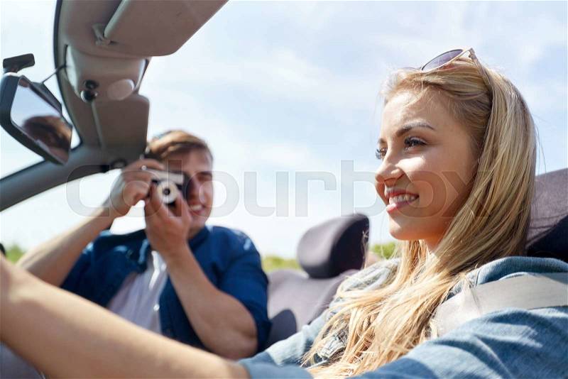 Leisure, road trip, travel and people concept - happy couple driving in cabriolet car and taking picture by film camera, stock photo