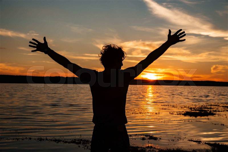 Happy man silhouette with hands up on the sunset background at the beach, stock photo
