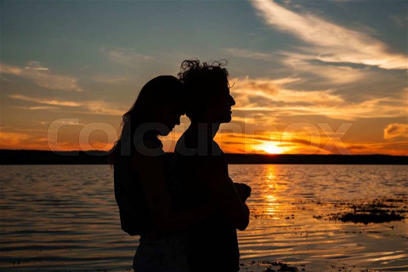 Silhouette of happy young couple hugging near the sea on sunset, stock photo