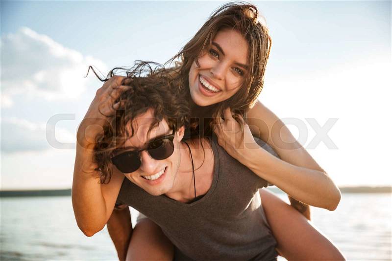 Young happy smiling couple in love piggyback at the beach, stock photo