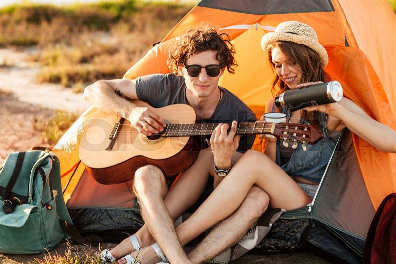 Portrait of a man playing guitar for his girlfriend camping at the beach, stock photo