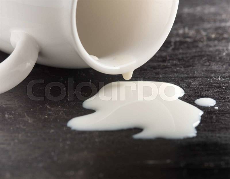 Milk spilled from glass on dark wooden, stock photo