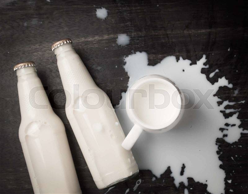 Milk bottle and Milk spilled on dark wood,top view, stock photo