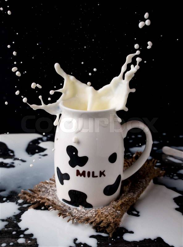 Splash of milk from the milk glass with cow camouflage on dark background, stock photo