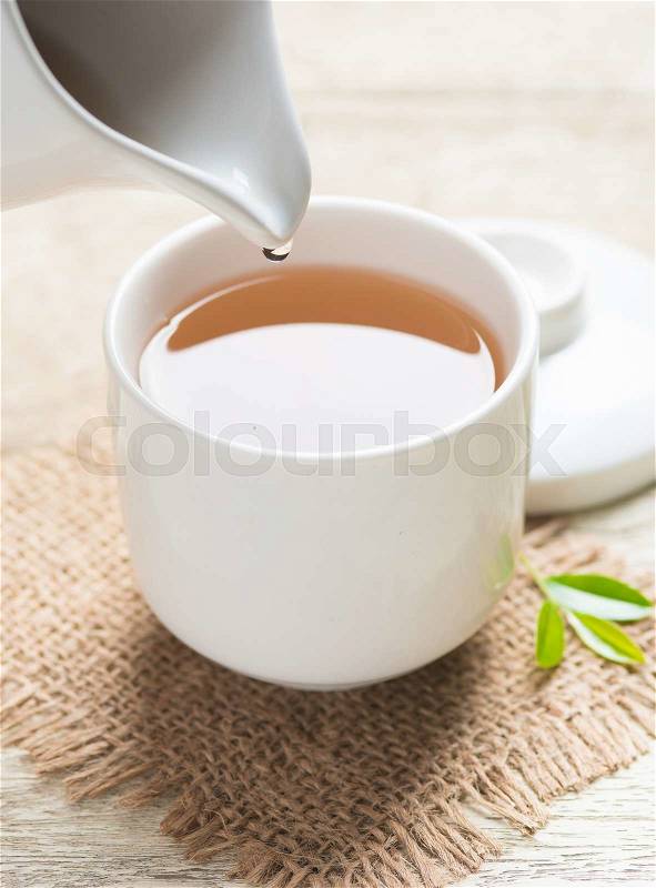 Pouring tea from jug to cup of tea and tea leaves on wooden , stock photo