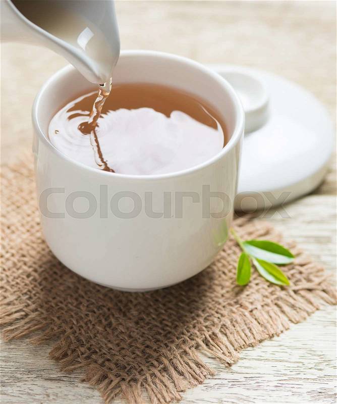Pouring tea from jug to cup of tea and tea leaves on wooden , stock photo