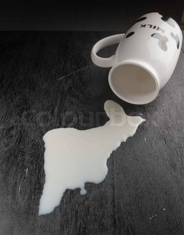 Milk spilled from glass on dark wooden, stock photo