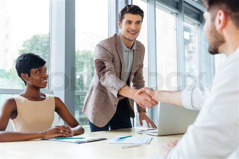 Happy successful young business people shaking hands in office, stock photo