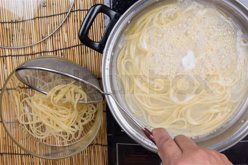 Spaghetti lifted on of cold water with colander / cooking spaghetti concept, stock photo