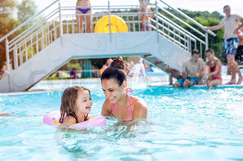 Young beautiful mother in bikini playing with her daughter in inflatable ring in swimming pool in aqua park. Summer heat and water, stock photo