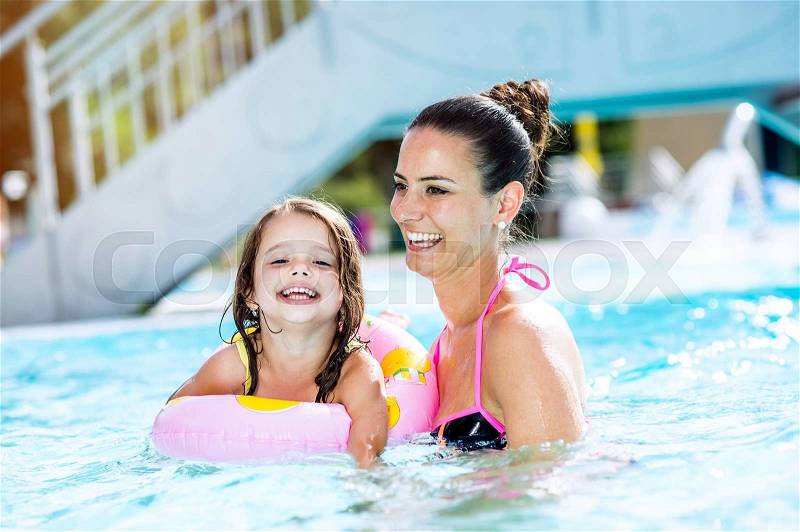 Young beautiful mother in bikini playing with her daughter in inflatable ring in swimming pool in aqua park. Summer heat and water, stock photo
