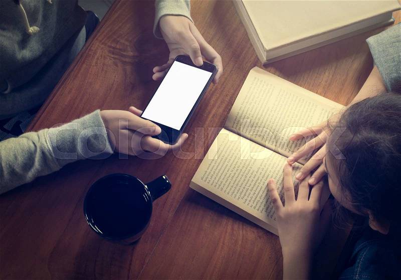 Girl reading a book and another girl holding smart phone on wooden table with coffee cup, stock photo