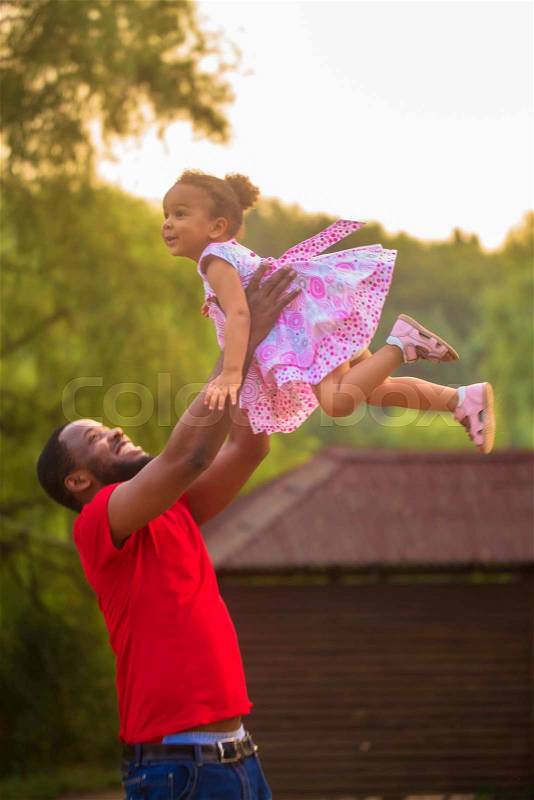 Cute black father and baby girl playing together. Baby flying up in the father's hands, stock photo