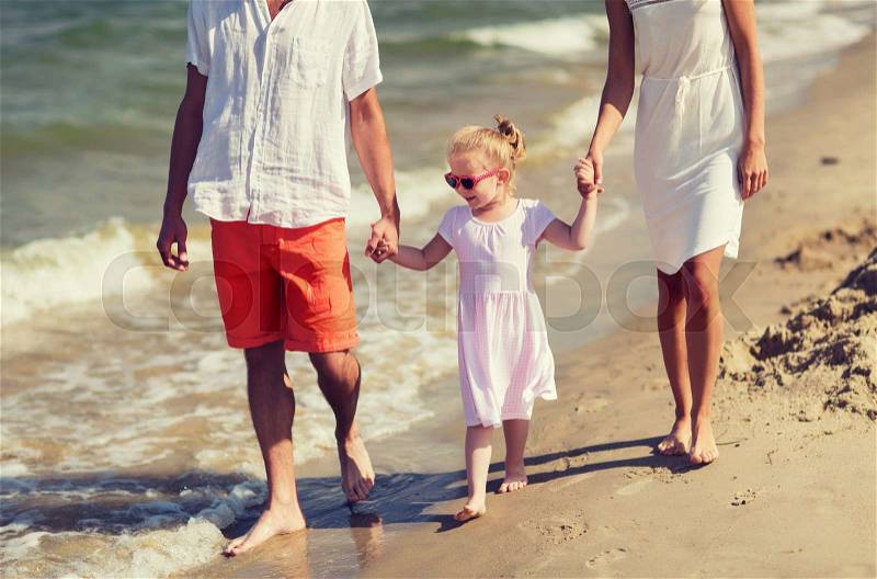 Family, vacation, adoption and people concept - happy man, woman and little girl in sunglasses walking on summer beach, stock photo