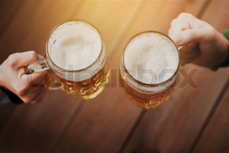 People, leisure and drinks concept - close up of male hands clinking beer mugs at bar or pub, stock photo