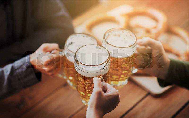 People, leisure and drinks concept - close up of hands clinking beer mugs at bar or pub, stock photo