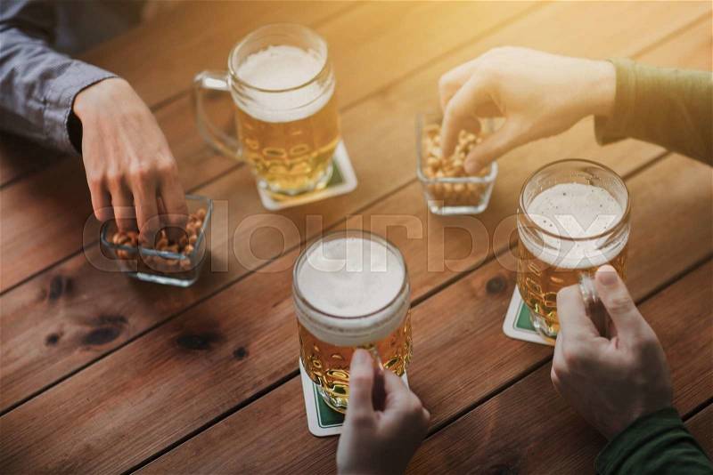 People, leisure and drinks concept - close up of male hands with beer mugs and peanuts at bar or pub, stock photo