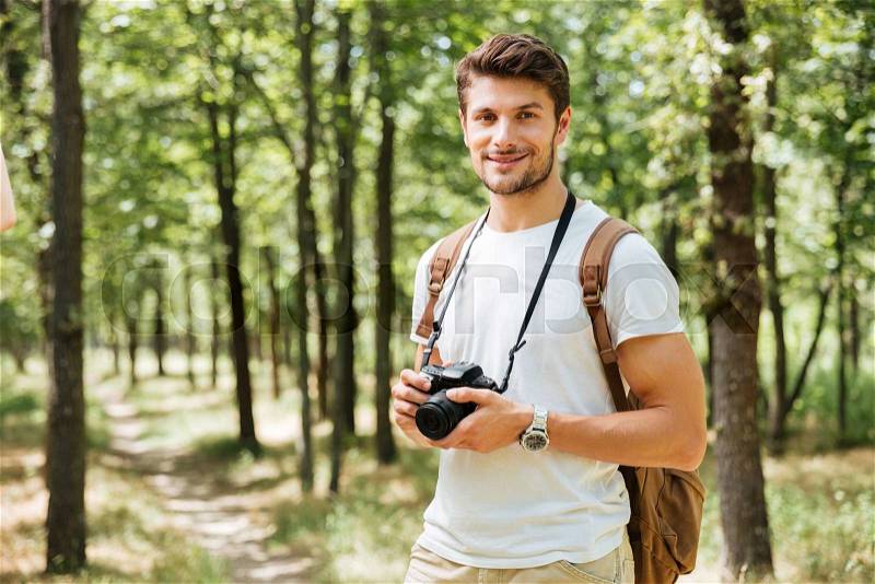 Happy young man photographer standing and holding modern photo camera outdoors, stock photo