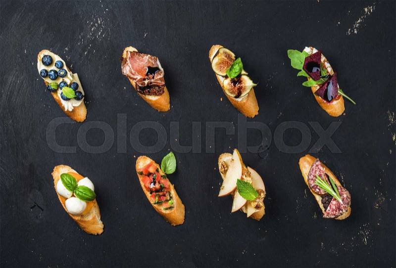 Italian crostini with various toppings on black plywood background, top view, stock photo