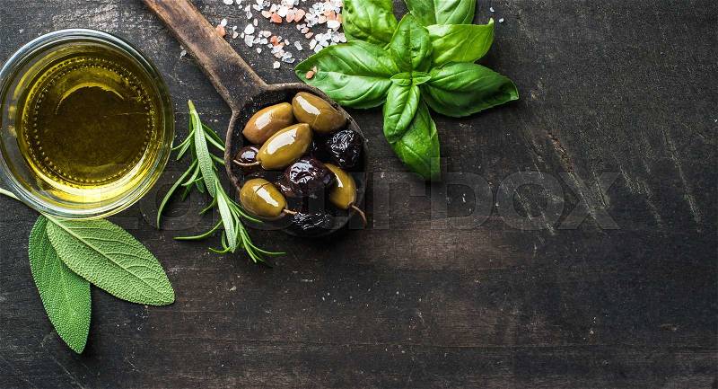 Green and black Mediterranean olives in old cooking spoon with olive oil and herbs over dark rustic wooden background, top view, copy space, stock photo