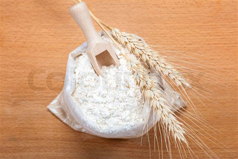 Flour in a canvas bag and wheat ears on a wooden background, stock photo