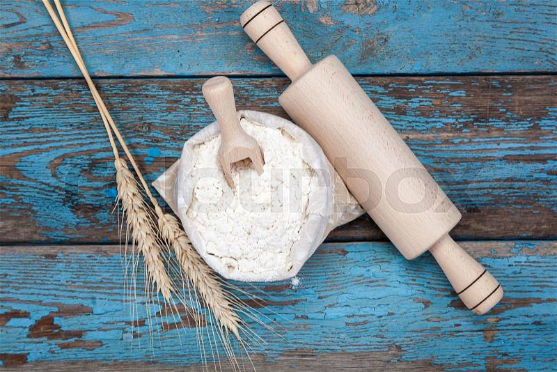 Flour in a canvas bag and wheat ears on a blue wooden background, stock photo
