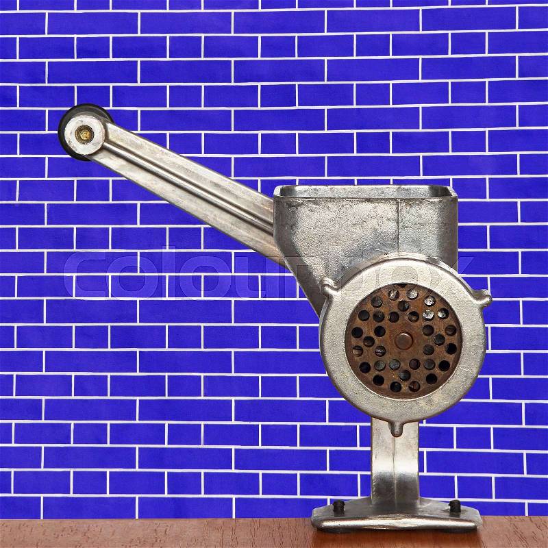 Old meat grinder on blue brick wall background taken closeup, stock photo
