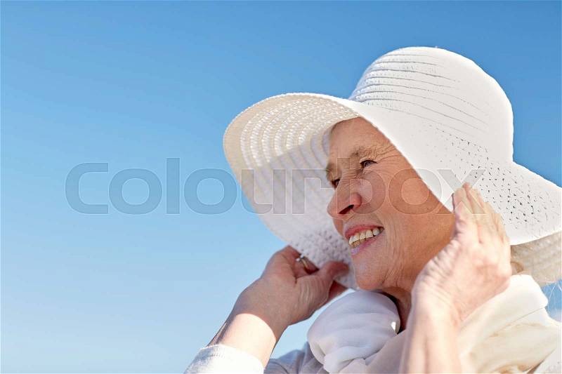 Age, leisure and people concept - happy senior woman in sun hat on summer beach, stock photo