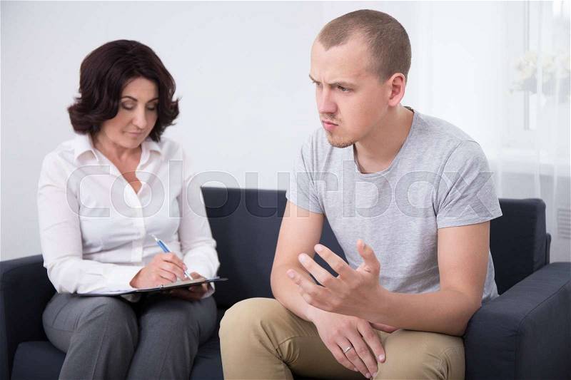 Psychotherapy concept - young sad man talking about his problems with psychotherapist or psychologist, stock photo