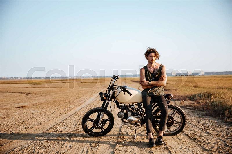 Young brutal man in black leaning on a motorcycle, stock photo