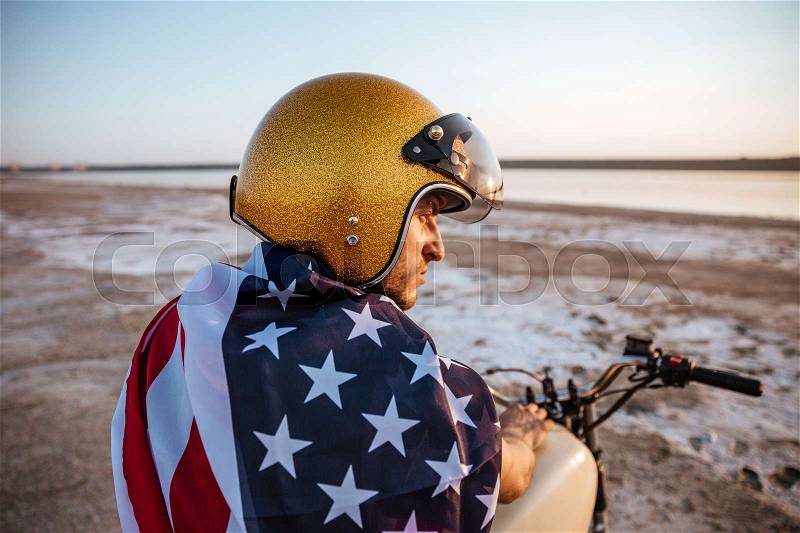 Close up portrait of a brutal man wearing golden helmet and american flag sitting on motorcycle, stock photo