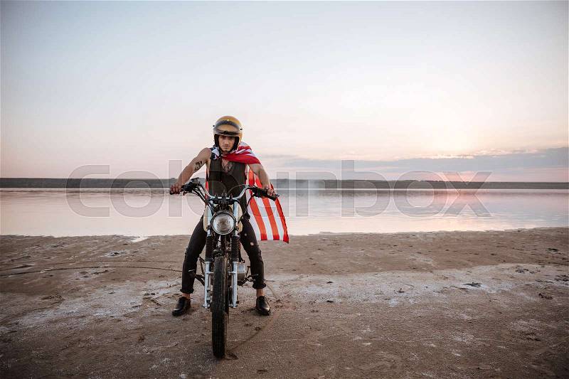 Young brutal man in golden helmet and american flag cape driving retro motorcycle, stock photo