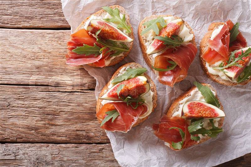 Bruschetta with figs, prosciutto, arugula and cream cheese close-up on the table. horizontal view from above , stock photo