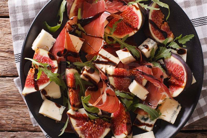 Salad with figs, prosciutto, cheese and arugula close-up on a plate on the table. horizontal view from above , stock photo