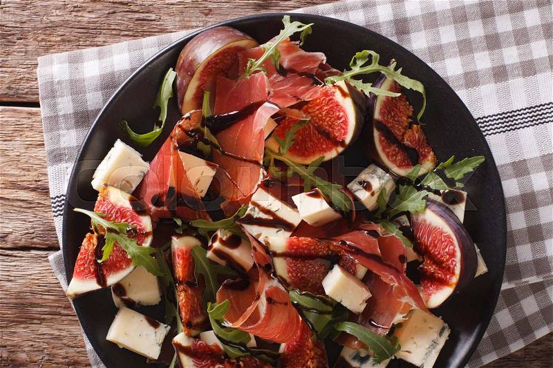 Salad with figs, cheese, prosciutto and arugula dressed with balsamic sauce on a plate on the table. horizontal view from above , stock photo