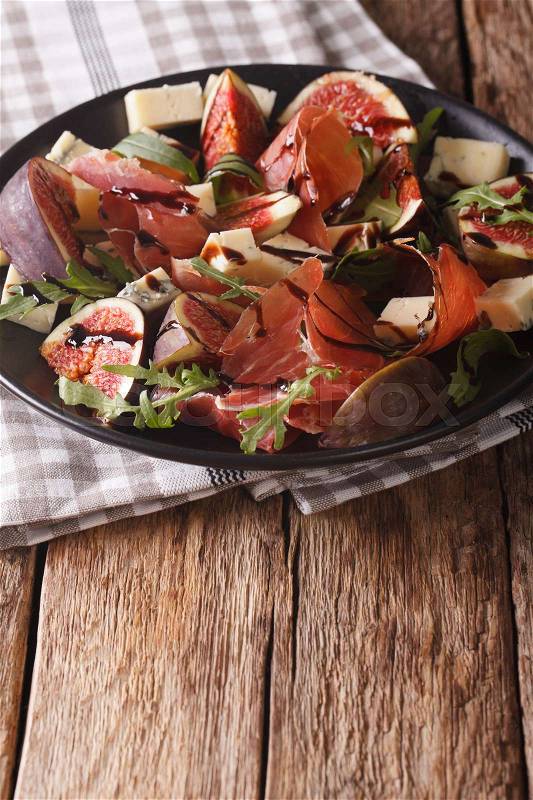 Salad with figs, cheese, prosciutto and arugula dressed with balsamic sauce on a plate on the table. vertical\, stock photo