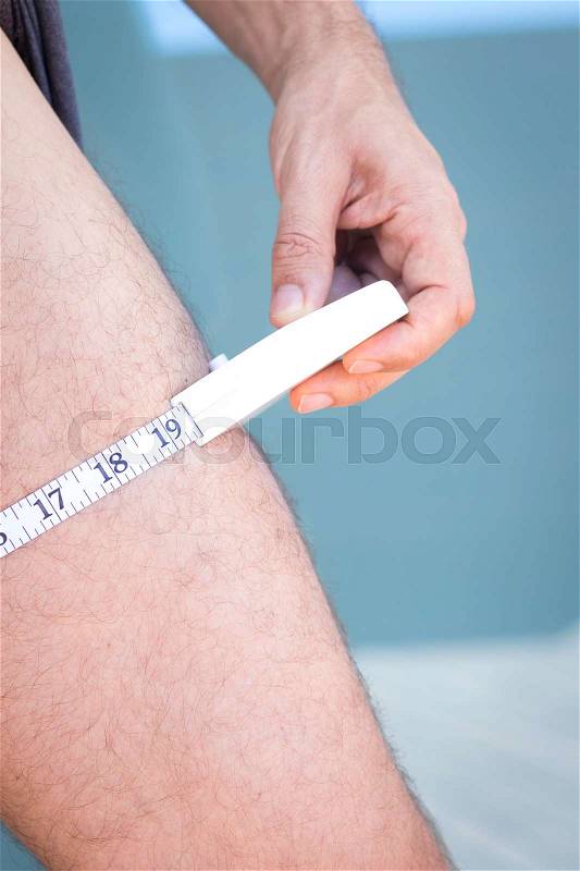 Slim attractive young man using measuring tape to measure weight loss and muscle on leg, stock photo