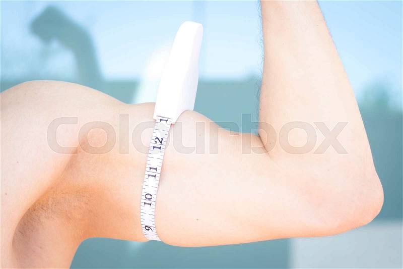 Slim attractive young man using measuring tape to measure weight loss o upper arm bicep and tricep, stock photo
